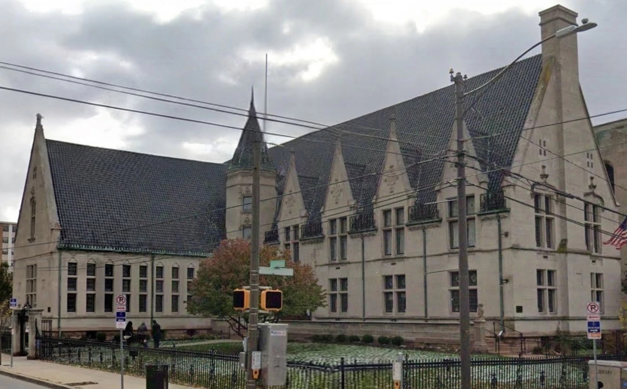 The library today: the same Gothic limestone front and slate roof behind its iron fence, with traffic signals and street signs across the corner.