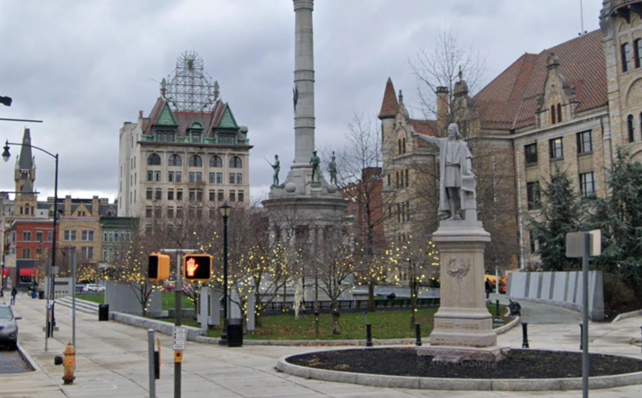 The Square today: the memorial column still on its plinth among bare trees, the courthouse and its clock tower to the right, parked cars along the kerb.